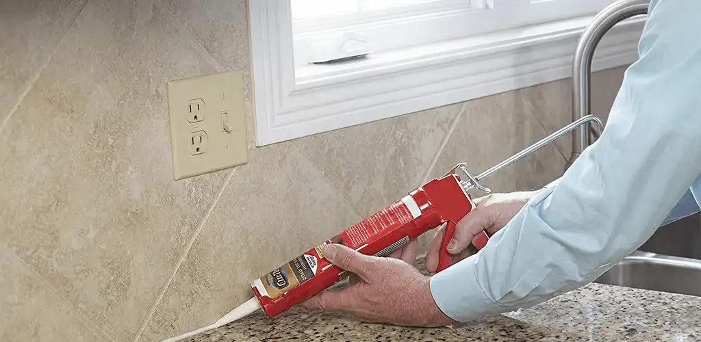 Handyman applying caulk along a kitchen backsplash and countertop seam in Fort Lauderdale, FL