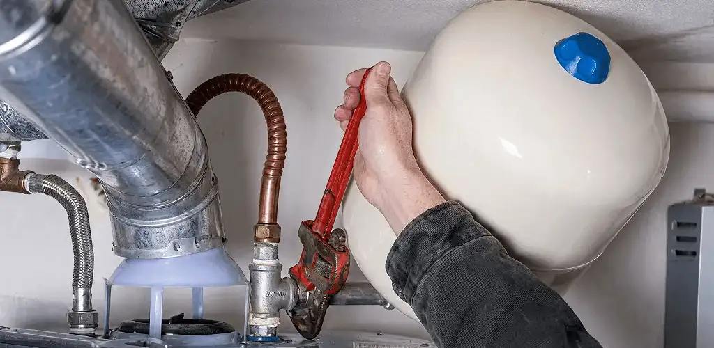 Water heater repair technician tightening plumbing connections near a tank unit in Fort Lauderdale, FL